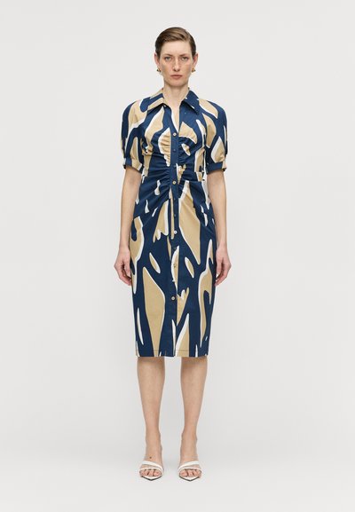 Robe boutonnée bleu marine avec des motifs abstraits beiges et blancs. Elle possède des manches bouffantes courtes, une taille cintrée et une longueur au genou.