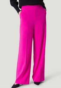 Pantalones de pierna ancha fucsias con una textura suave, cintura alta y bolsillos laterales, combinados con tacones de punta negra.