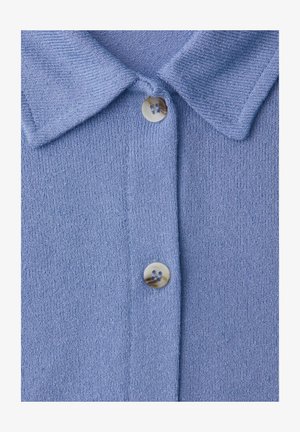 Vaaleansininen neulospaitapaita, jossa on kaulus ja edessä keskellä kiinnitettynä kaksi näkyvää kermaan vivahtavaa nappia.