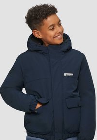 Giubbotto impermeabile blu navy con cappuccio, polsini elastici, tasche frontali e un'etichetta con logo. Texture liscia, cerniera chiusa e chiusura sicura.
