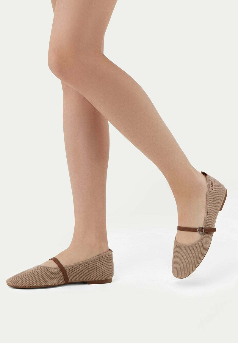 Ballettskor i ljusbeige ribbat material med ett brunt band och en cirkulär accent. Lågprofil design med en mjuk textur.