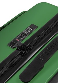 Groene harde koffer met een zwarte rits, combinatie slot en reliëfmerknaam; gladde textuur met een strakker ontwerp.