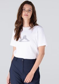 Witte katoenen t-shirt met korte mouwen, voorzien van een grijs grafisch ontwerp aan de voorkant. Gecombineerd met marineblauwe broek met streepjes.