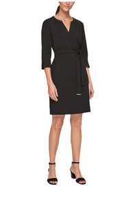 Robe noire en tissu lisse, avec un décolleté en V, des manches trois-quarts et une ceinture à la taille. Dotée d'un accent argenté subtil.