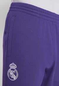 Calças de sweat em roxo feitas de um tecido suave, com uma cintura canelada, bolsos laterais e um logo bordado do Real Madrid em branco.