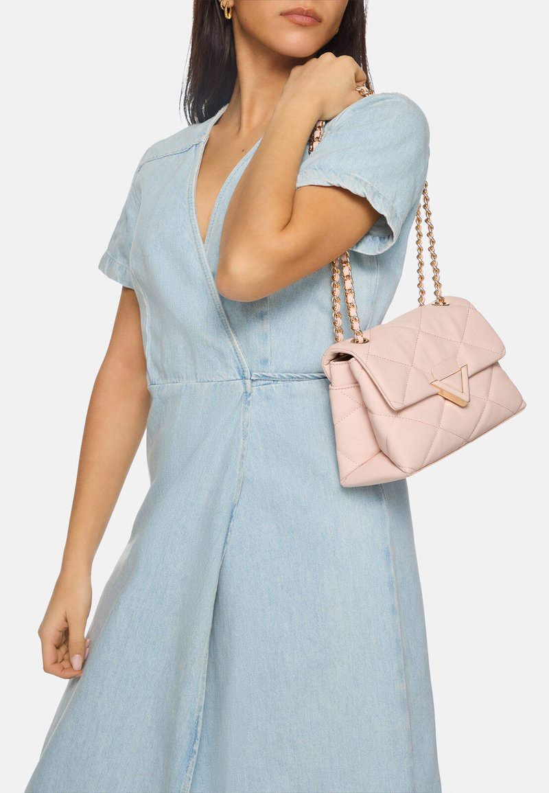 Borsa a tracolla rosa trapuntata con dettagli in metallo dorato e catena, tenuta da una persona che indossa un vestito di jeans azzurro chiaro.