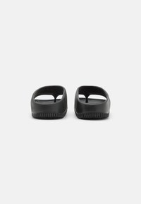 Mustat kumiset liukuvaatteet avonaisella muotoilulla, jossa on tasapohja ja sileä pinta, joka on haitari minimalistiselle muodolle.