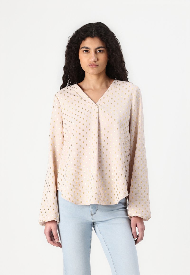 Blusa a maniche lunghe in morbido tessuto rosa pallido con scollo a V, caratterizzata da un motivo a quadrati dorati. Il design è morbido con orlo curvo.