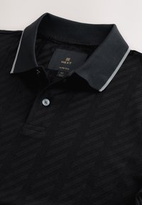 Zwart slim-fit poloshirt met een gestructureerd chevronpatroon, een contrasterende kraag met grijze accenten en een drieknops beleg.