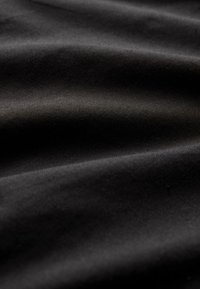 Schwarzer Stoff, in Falten gelegt, zeigt eine glatte Textur mit leichtem Glanz. Die Webart ist dicht und gleichmäßig, was die Haltbarkeit erhöht.