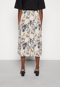 Blommig midikjol med en krämfärgad bas och mönster i blått, rosa och brunt. Den har en rak skärning och är kombinerad med klackskor med blockheel.