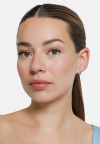 Boucles d'oreilles en forme de cerceau en or avec un détail texturé, le modèle présente des cheveux bruns raides, un maquillage léger et un teint lisse, portant un haut bleu.