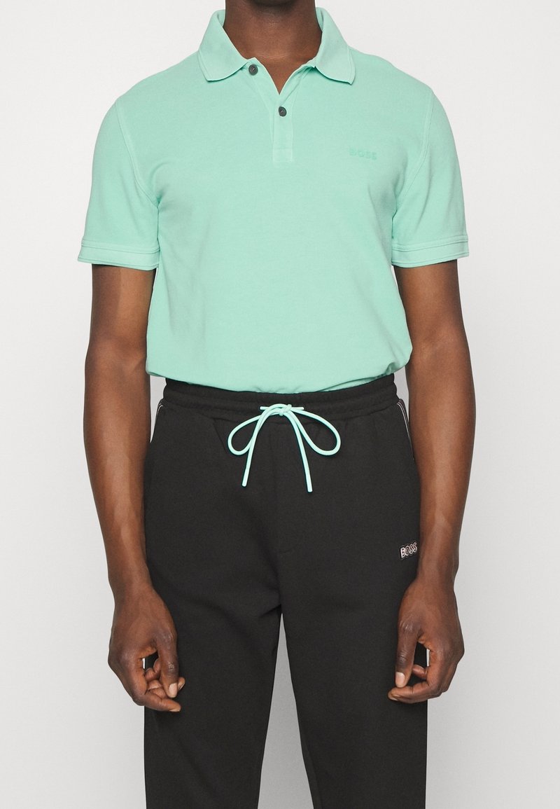 Polo vert menthe avec une patte de boutonnage à trois boutons et pantalon noir avec un cordon de serrage bleu clair et le logo "BOSS" sur la jambe.