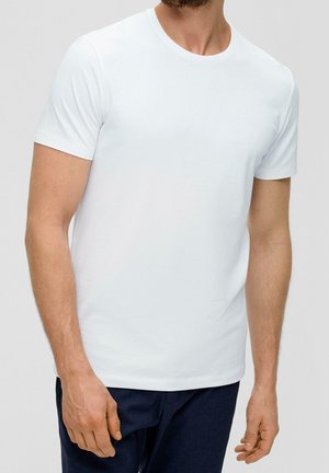 Mann trägt ein schlichtes weißes kurzärmeliges T-Shirt und dunkle Hose, gezeigt vom Hals bis zur Hüfte vor einfachem Hintergrund.