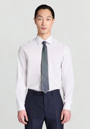 Chemise blanche à col pointu, associée à une cravate bleue texturée. La coupe est ajustée, assortie à un pantalon bleu marine foncé.