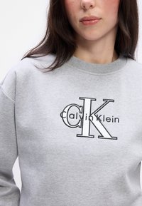 Γκρι φούτερ με μαύρη κεντητή λογότυπο "Calvin Klein" και μεγάλο σχέδιο "CK". Μαλακό ύφασμα και στρογγυλή λαιμόκοψη.