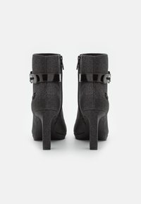 Bottines noires à talons hauts avec une finition texturée, dotées d'une bride en cuir verni brillant et d'une boucle décorative sur le côté.
