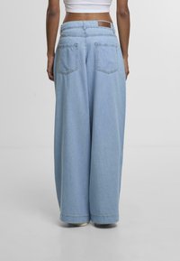 Light blue denim wide-leg pants with a high waist, featuring two back pockets and a labeled waist patch. Smooth texture and loose fit.