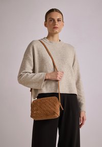 Torebka crossbody z plecionego zamszu w jasnobrązowym kolorze, o prostokątnym kształcie, z zamknięciem na zamek błyskawiczny i regulowanym paskiem. Miękka tekstura i minimalistyczny design.