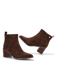 Botas hasta el tobillo de ante marrón con punta afilada, un tacón apilado de altura media y un botón de acento dorado en el lateral. Superficie texturizada y diseño elegante.