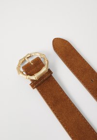 Brauner Wildledergürtel mit strukturiertem Finish und einer goldenen, bambusförmigen Schnalle. Das Gürtelende ist verjüngt und verfügt über eine Naht entlang der Kanten.