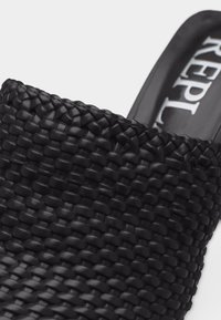 Μαύρο πλεκτό δερμάτινο παπούτσι mule με στρογγυλεμένη μύτη και ορατό όνομα επωνυμίας στην επιφάνεια ποδιού.