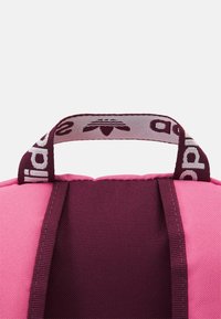 Rosa och vinröd väska med texturerad yta, utrustad med ett topphandtag med ett mönstrat band. Markant färgkontrast mellan sektionerna.