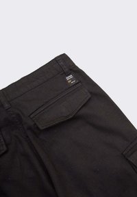 Pantalons cargo noirs en tissu texturé, avec une poche arrière et une étiquette logo cousue, présentant une forme rectangulaire et une taille standard.
