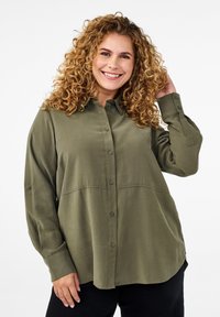 Olive green button-up shirt, lightweight fabric, long sleeves with button cuffs, curved hemline, featuring a stitched panel across the chest.