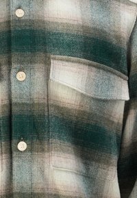 Flanellen shirt met een groen, bruin en crème ruitpatroon. Het heeft een knopenfront en een borstzak van een zachte, gestructureerde stof.