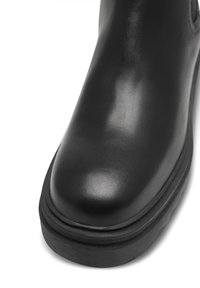 Botín de cuero negro con un acabado liso, puntera redonda y suela gruesa de goma negra. Diseño minimalista sin adornos.