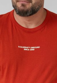 Rotes Baumwoll-T-Shirt mit Rundhalsausschnitt. Mit weißem Text "S.OLIVER® UNBOUND SINCE 1969" über der Brust. Weicher Stoff.