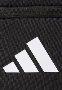 Trzy białe diagonalne paski o rosnących rozmiarach na teksturowanej czarnej tkaninie, tworzące logo marki odzieżowej sportowej.