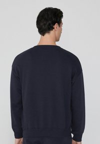 Sudadera navy de mangas largas, con puños y dobladillo acanalados. Material suave con un diseño sencillo, mostrando la vista posterior y sin marcas visibles.