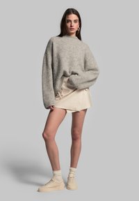 Übergroßer grauer gestrickter Pullover, schlichte beiger Rock mit Kordelzug und cremfarbene Plateausneaker. Glatte Textur und entspannte Silhouette.