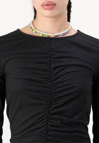 Črn dolg rokav s nabranim tekstilom spredaj, oblečen z barvitim beaded ogrlico z nasmejanimi obrazi.