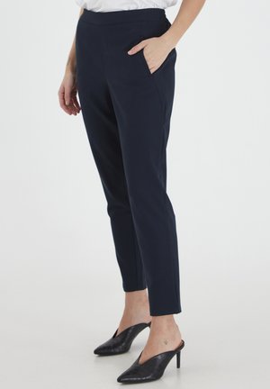 Pantaloni tapered blu navy realizzati in tessuto morbido, con una vestibilità slim, tasche laterali e vita media. Combinati con mule neri con tacco.