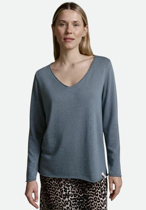 Helleblaue Langarmbluse mit V-Ausschnitt und strukturiertem Stoff, kombiniert mit einem Leopardenmuster-Rock, der ein Seitenlabel-Detail aufweist.