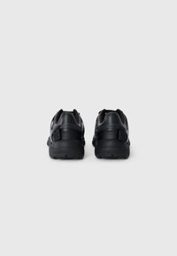 Black athletic shoes with a textured sole, cushioned heel, and dual strap closures. Minimalist design featuring a sleek profile.