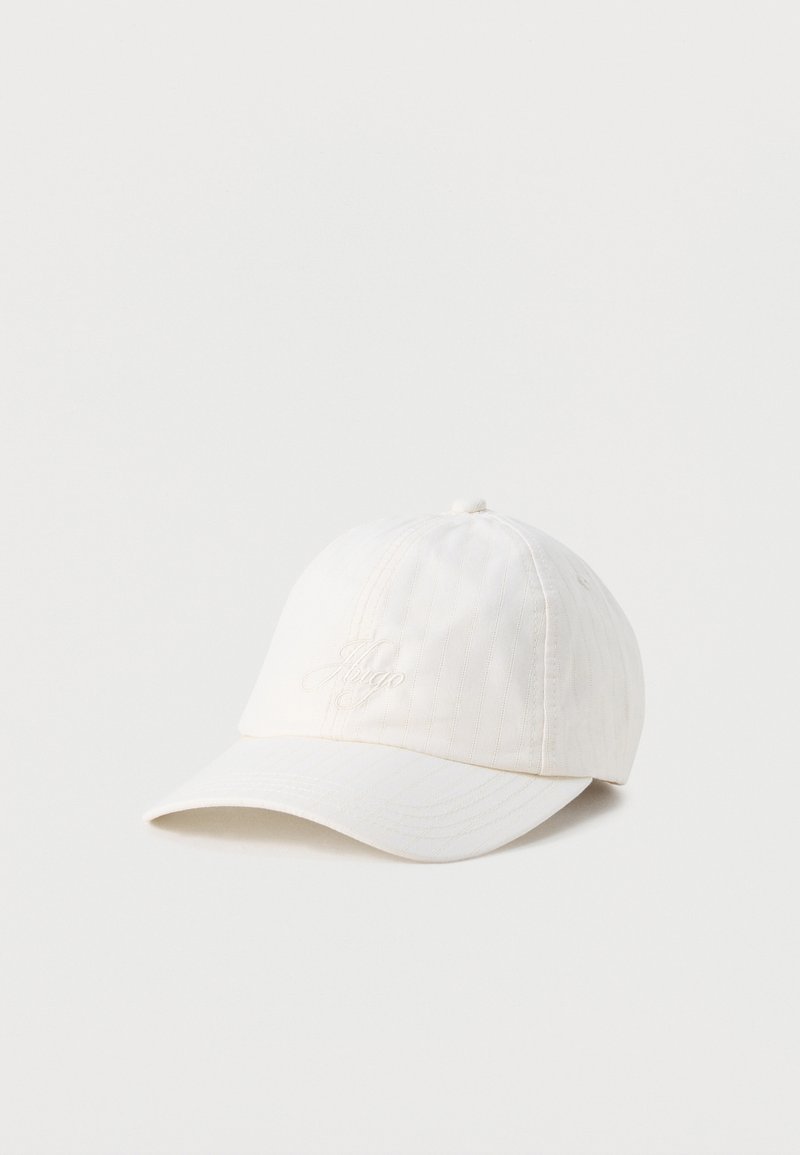 Casquette de baseball blanche avec des rayures verticales subtiles et le logo "Hugo" brodé, présentée sur un fond uni clair.