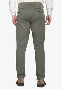 Pantaloni verdi oliva, con texture e taglio slim, dotati di due tasche posteriori e orli regolabili, abbinati a stivali in camoscio marroni.