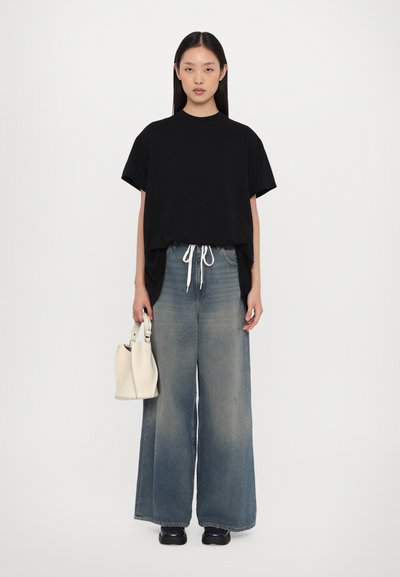 T-shirt nera oversize con maniche corte, jeans a gamba larga blu chiaro, cintura bianca con lacci e una piccola borsa bianca. Scarpe nere.