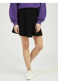 Musta pehmeästä kankaasta valmistettu kellohame, jossa on liehuva malli ja joka ulottuu polven yläpuolelle, yhdistetty valkoisiin lenkkareihin ja violettiin neulepaitaan.