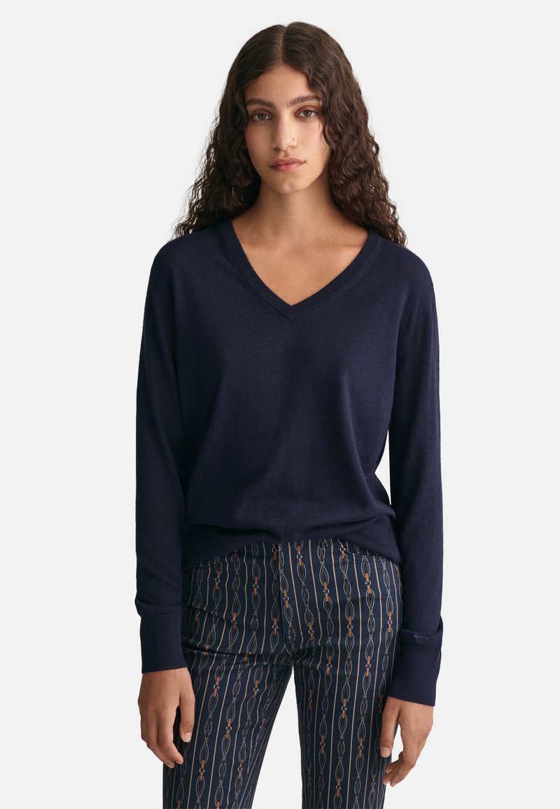 Marineblauer V-Ausschnitt-Pullover aus weichem Strick mit langen Ärmeln und gerippten Bündchen, kombiniert mit gemusterten, schmal zulaufenden Hosen in dunklen und hellen Farben.