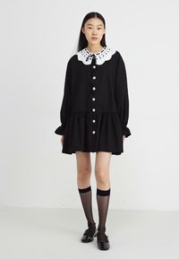 Rochie neagră cu mâneci lungi, cu o guler din dantelă albă și nasturi mari, având o fustă în volane. Pur și simplu cu ciorapi până la genunchi și pantofi negri.