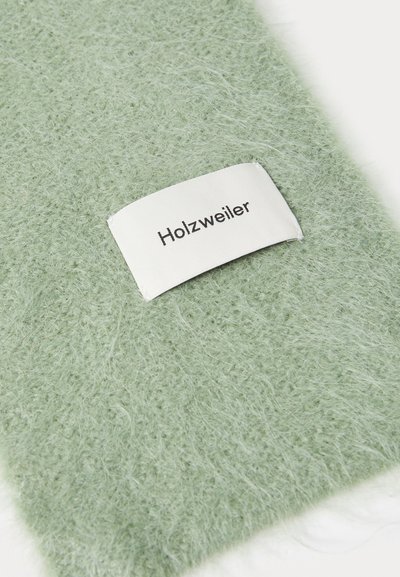 Pehmeä, vaaleanvihreä karheapintainen kangas, jossa on valkoinen "Holzweiler"-merkki ommeltuna yhteen reunaan.