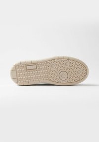 Suela de una zapatilla en caucho beige claro, que presenta un patrón texturizado con acentos circulares y en forma de diamante, etiquetada "D.A.T.E."