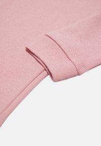Manga de sudadera de color rosa claro con un puño acanalado. La tela parece suave y ligeramente texturizada, resaltando el acabado liso y los detalles de las costuras.