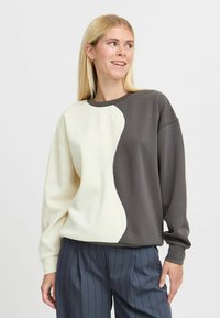 Sweatshirt featuring a split design with a cream side and a dark gray side, made of smooth fabric. Ribbed neckline and cuffs.