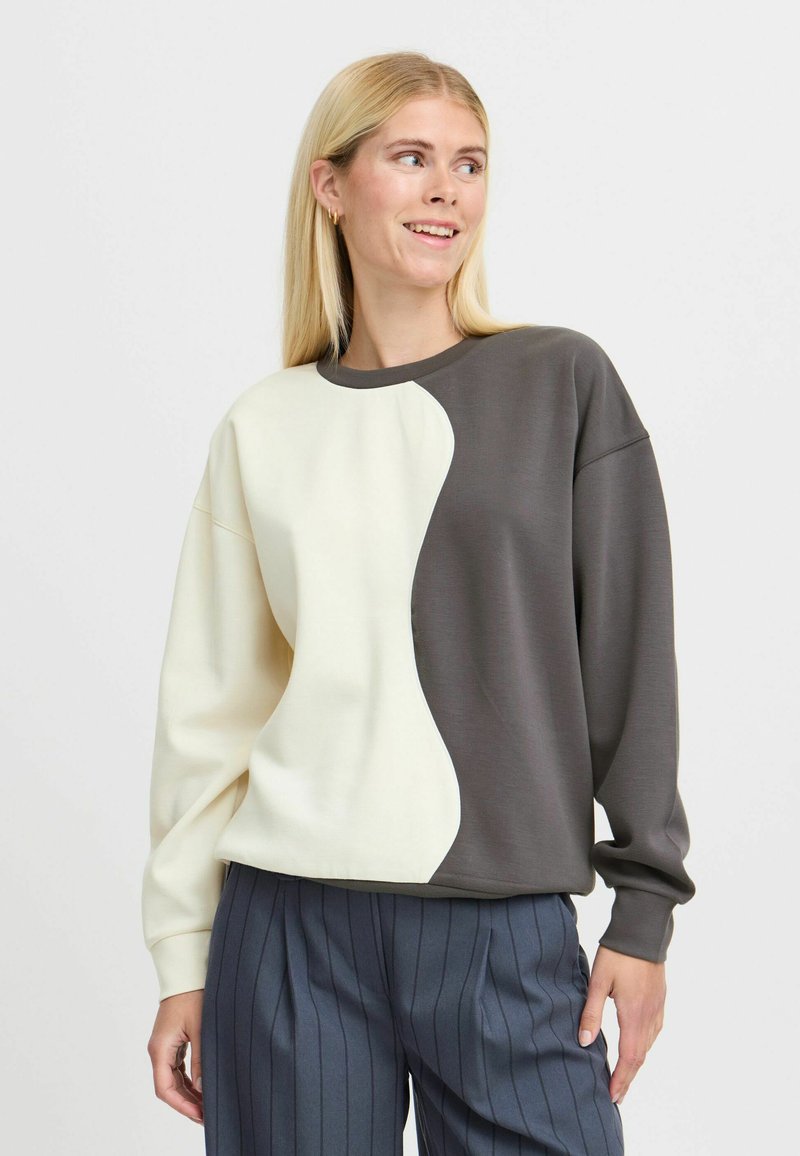 Sweatshirt featuring a split design with a cream side and a dark gray side, made of smooth fabric. Ribbed neckline and cuffs.